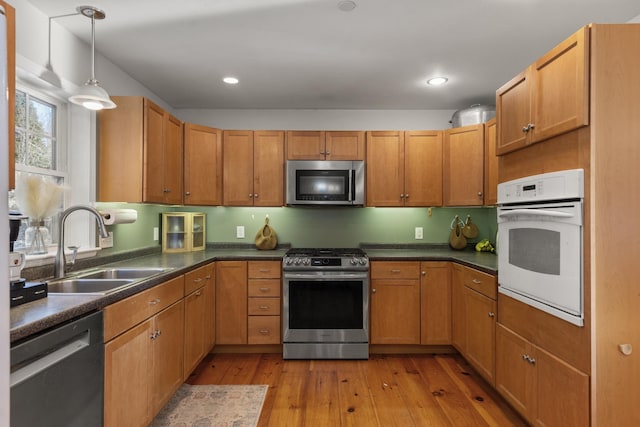 kitchen with appliances with stainless steel finishes, sink, pendant lighting, and light hardwood / wood-style floors