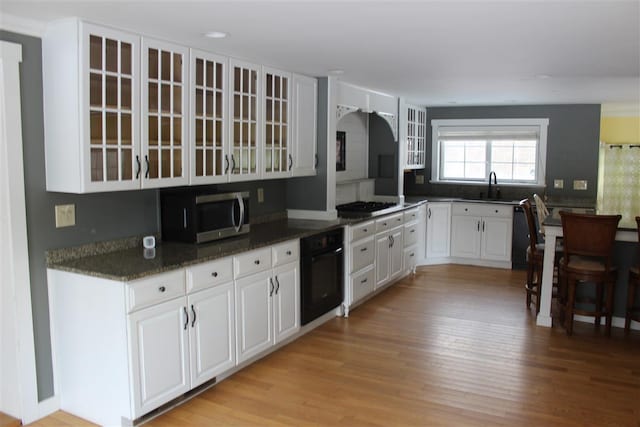 kitchen featuring sink, appliances with stainless steel finishes, white cabinetry, dark stone counters, and light wood-type flooring