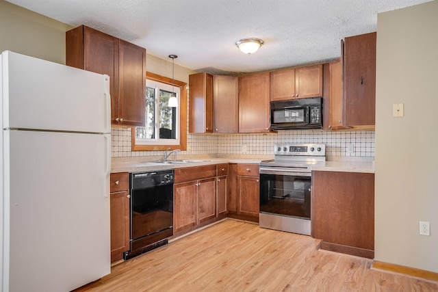 kitchen featuring sink, a textured ceiling, pendant lighting, light hardwood / wood-style floors, and black appliances