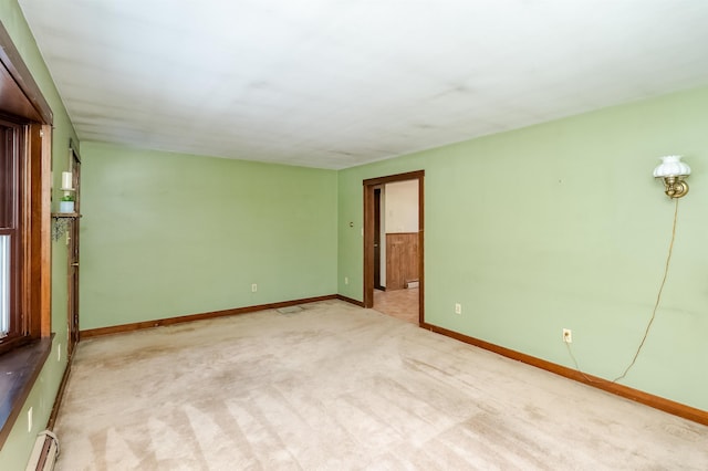 empty room featuring a baseboard heating unit and light colored carpet