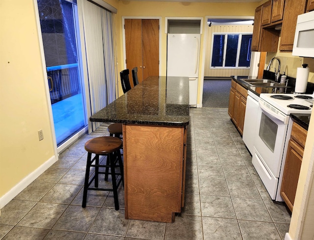 kitchen featuring sink, white appliances, a kitchen island, a kitchen bar, and dark stone counters