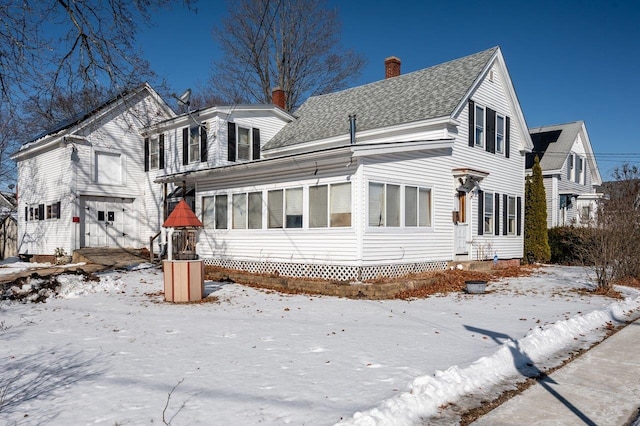 snow covered house featuring a shingled roof, a chimney, a garage, and a sunroom