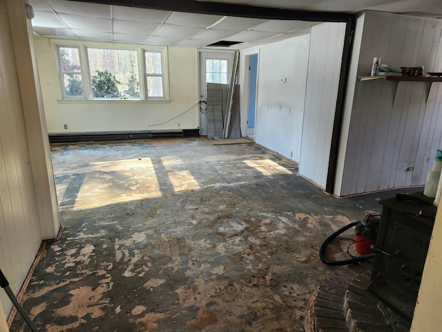 basement with a drop ceiling, a baseboard heating unit, and wood walls