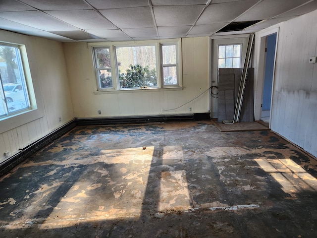 empty room featuring baseboard heating, wood walls, and a drop ceiling