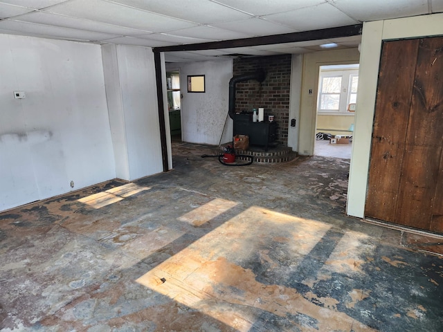 basement featuring a paneled ceiling and a wood stove