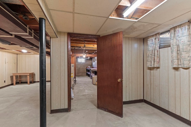 basement with a paneled ceiling, gas water heater, and wood walls