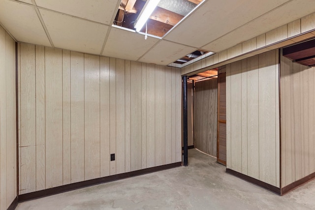 basement featuring wooden walls and a drop ceiling