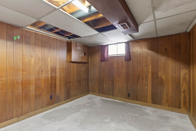 basement featuring a paneled ceiling and wooden walls