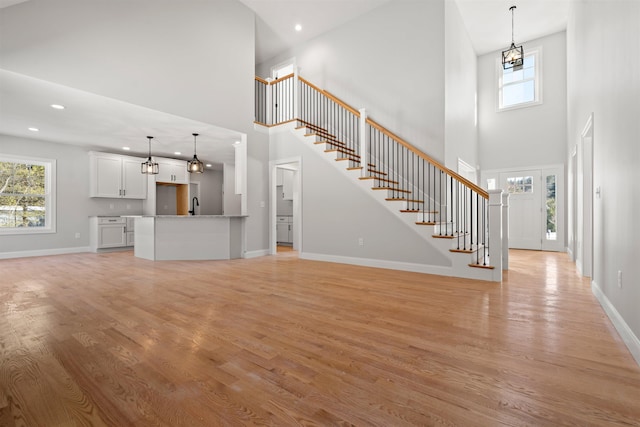 unfurnished living room with light wood-type flooring, a chandelier, and a high ceiling