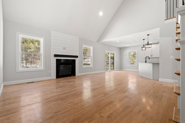 unfurnished living room with sink, high vaulted ceiling, and light hardwood / wood-style flooring