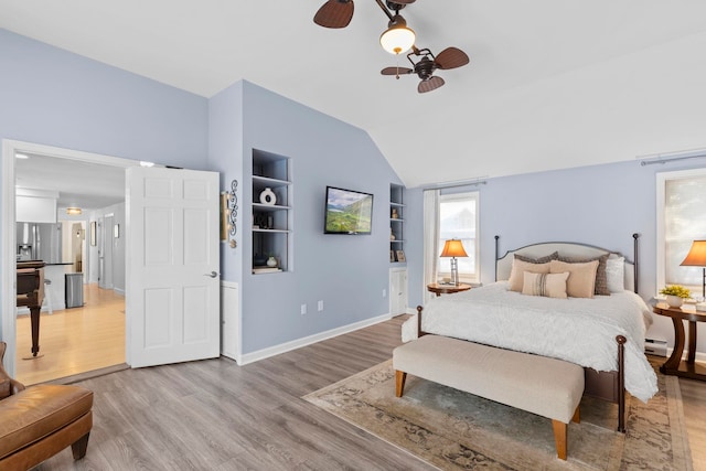 bedroom featuring vaulted ceiling, a baseboard heating unit, ceiling fan, stainless steel refrigerator with ice dispenser, and light hardwood / wood-style flooring