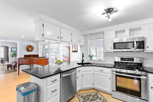 kitchen featuring sink, light wood-type flooring, kitchen peninsula, stainless steel appliances, and white cabinets