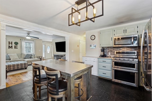 kitchen with ceiling fan with notable chandelier, decorative light fixtures, a kitchen breakfast bar, decorative backsplash, and stainless steel appliances