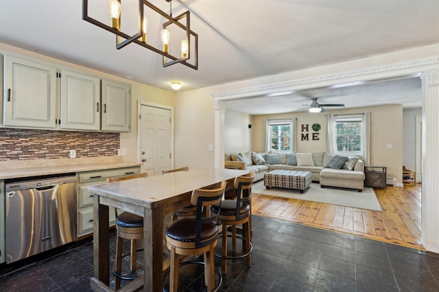 kitchen featuring ceiling fan with notable chandelier, pendant lighting, tasteful backsplash, dishwasher, and a breakfast bar area