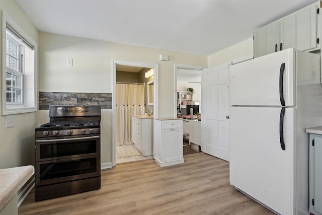 kitchen with white cabinetry, stainless steel range with gas cooktop, light hardwood / wood-style flooring, and white fridge