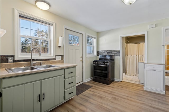 kitchen featuring sink, stainless steel gas range oven, light hardwood / wood-style floors, and green cabinets