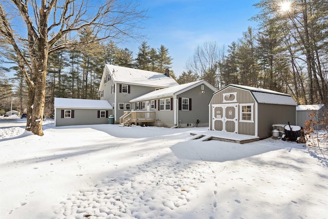 snow covered back of property featuring a storage shed and a deck