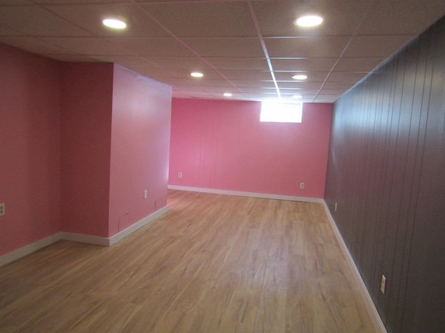 basement featuring a drop ceiling, wood-type flooring, and wooden walls