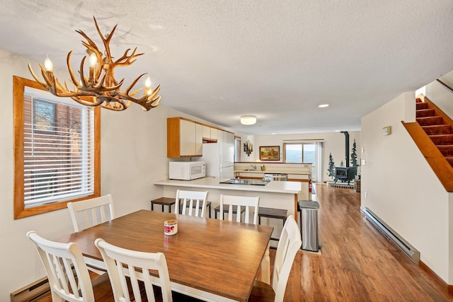 dining space featuring a baseboard radiator, light hardwood / wood-style floors, a textured ceiling, and a wood stove