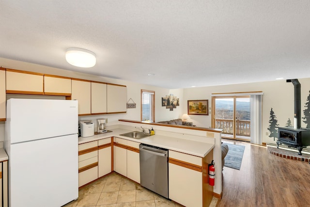 kitchen with stainless steel dishwasher, kitchen peninsula, white fridge, and a wood stove