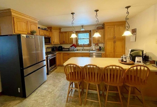 kitchen featuring appliances with stainless steel finishes, decorative light fixtures, sink, and a breakfast bar area