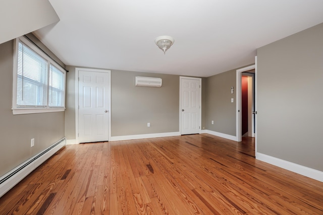 spare room featuring a baseboard radiator, an AC wall unit, and light wood-type flooring