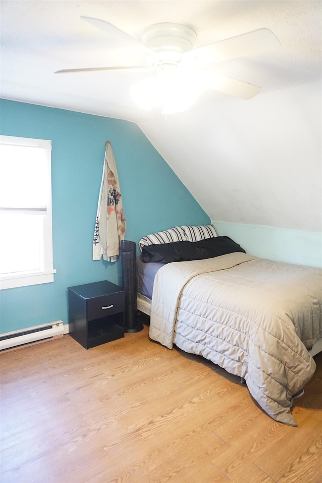 bedroom with vaulted ceiling, ceiling fan, hardwood / wood-style floors, and a baseboard heating unit