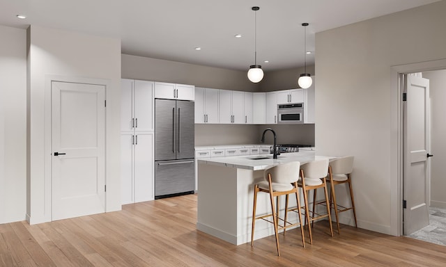 kitchen with a sink, stainless steel appliances, a kitchen bar, and light wood-style floors