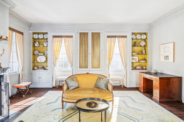 sitting room featuring built in shelves, a healthy amount of sunlight, crown molding, and dark wood-type flooring