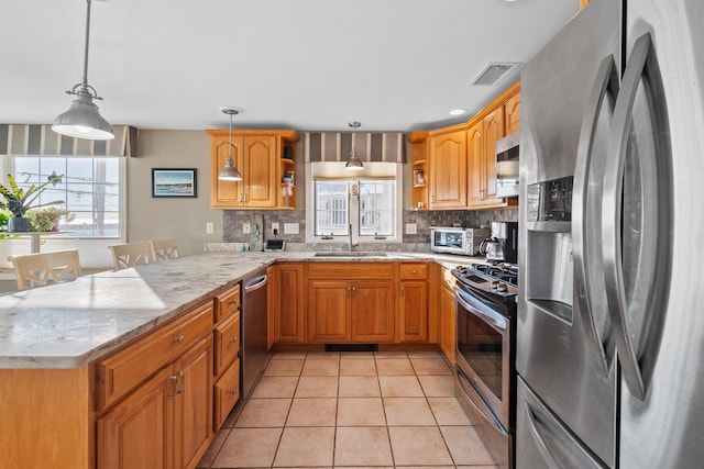 kitchen featuring appliances with stainless steel finishes, decorative light fixtures, a wealth of natural light, and kitchen peninsula