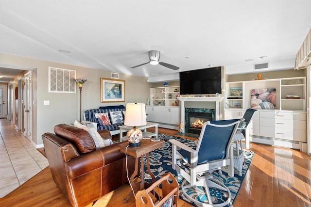 living room with a premium fireplace, light tile patterned flooring, a baseboard heating unit, and ceiling fan