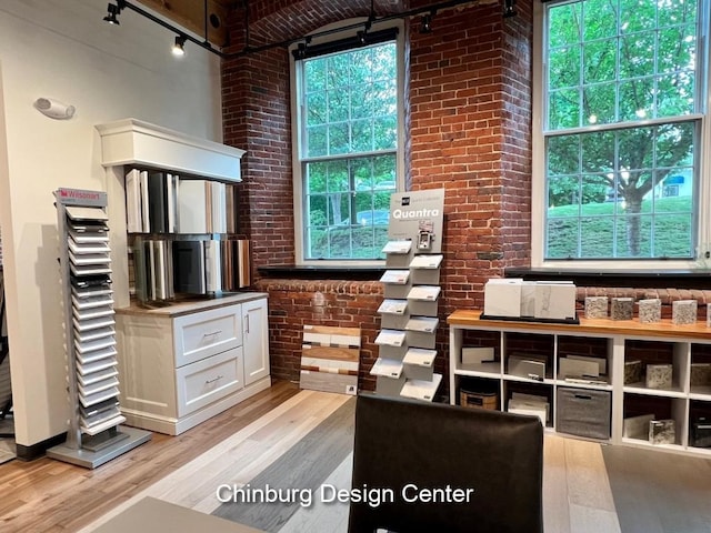 office with a towering ceiling, light hardwood / wood-style floors, rail lighting, and brick wall