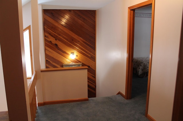 corridor featuring wooden walls and dark colored carpet