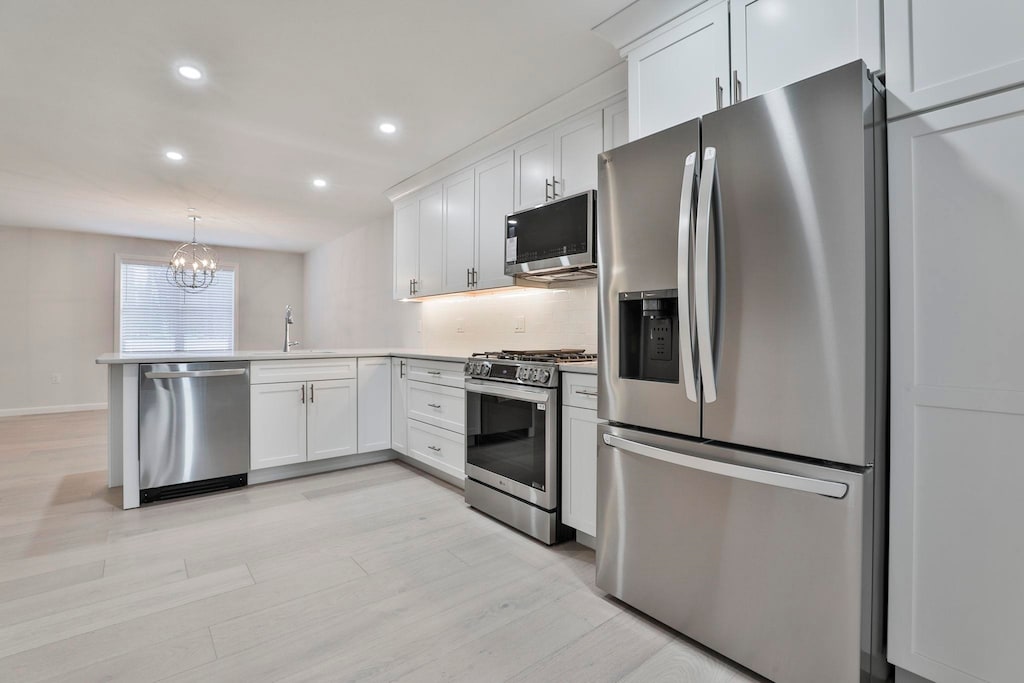 kitchen with white cabinetry, pendant lighting, stainless steel appliances, and a chandelier