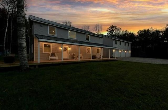 back house at dusk with a yard and covered porch