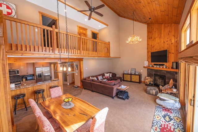 carpeted dining space with ceiling fan with notable chandelier, high vaulted ceiling, and wooden ceiling