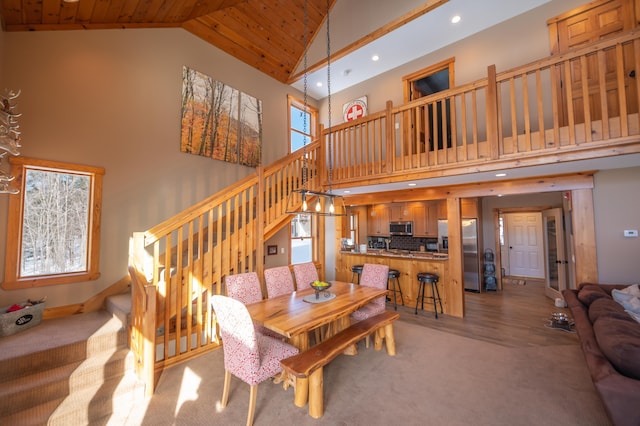 carpeted dining space featuring wood ceiling and high vaulted ceiling