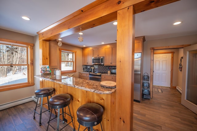 kitchen with light stone countertops, dark wood-type flooring, stainless steel appliances, and a breakfast bar area