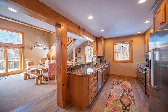 kitchen with sink, decorative light fixtures, dark stone countertops, appliances with stainless steel finishes, and dark hardwood / wood-style floors