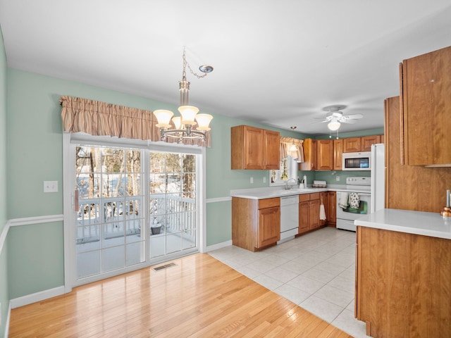 kitchen with light tile patterned floors, white appliances, sink, ceiling fan with notable chandelier, and decorative light fixtures