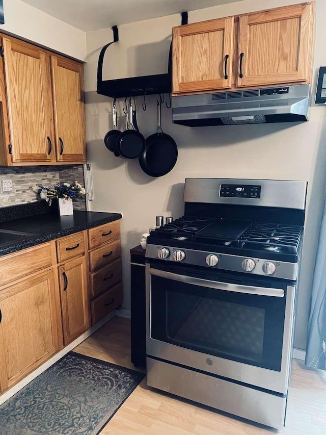 kitchen featuring stainless steel gas stove, decorative backsplash, and light wood-type flooring