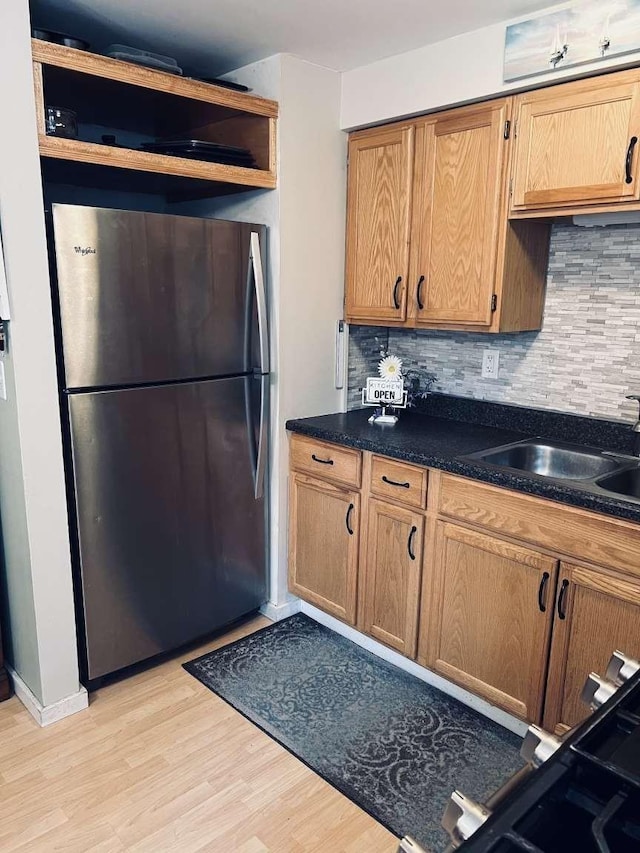 kitchen featuring stainless steel refrigerator, backsplash, sink, and light wood-type flooring