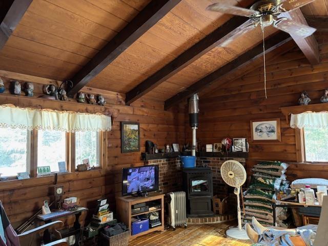 living room with wooden walls, radiator, lofted ceiling with beams, and a wood stove