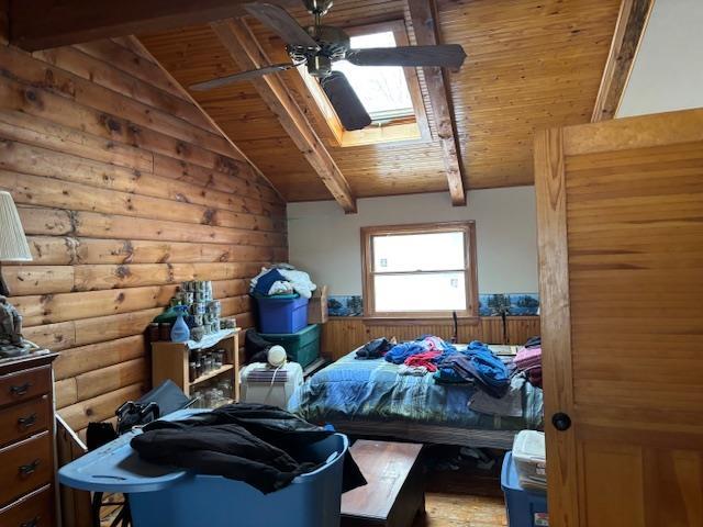 bedroom with log walls, wooden ceiling, and vaulted ceiling with skylight