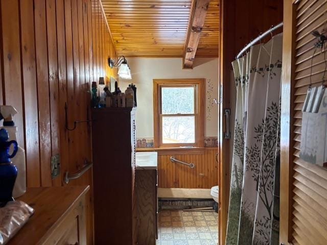 bathroom with wood ceiling, beam ceiling, a shower with curtain, toilet, and wood walls