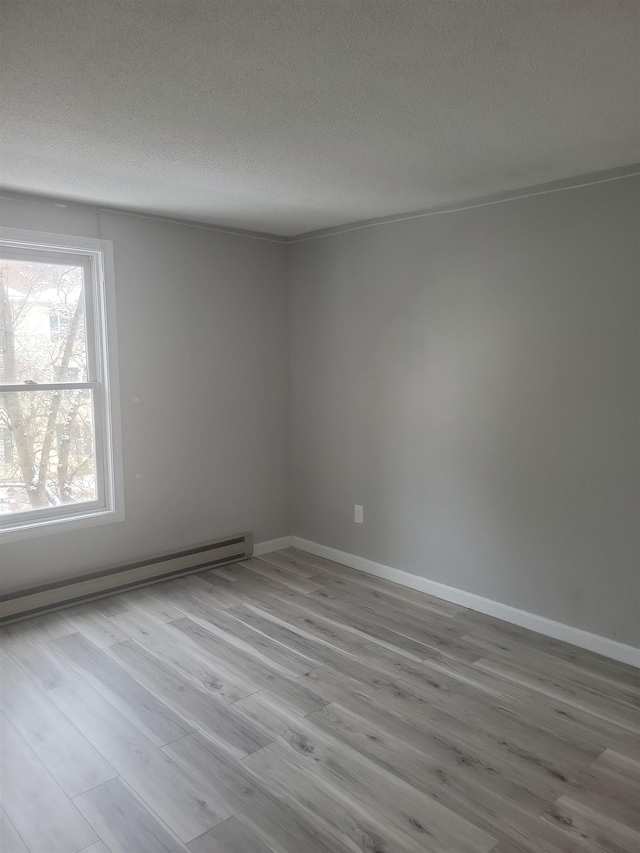 spare room with baseboard heating, light hardwood / wood-style floors, and a textured ceiling