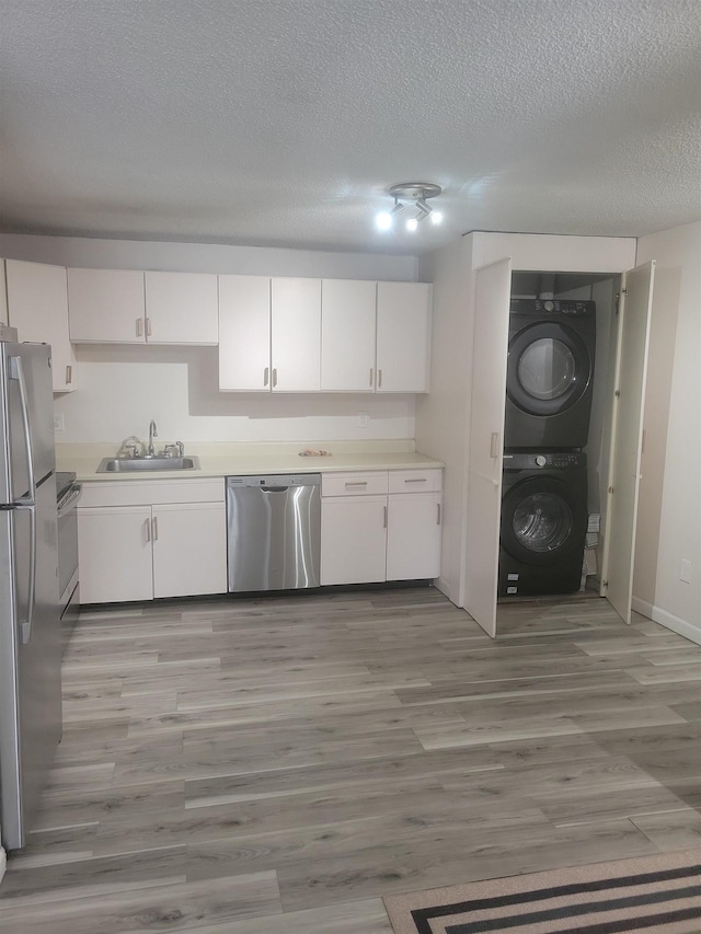 kitchen featuring sink, stainless steel appliances, stacked washing maching and dryer, light hardwood / wood-style floors, and white cabinets