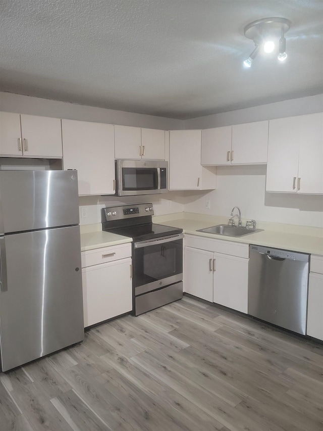 kitchen with stainless steel appliances, sink, light hardwood / wood-style flooring, and white cabinets