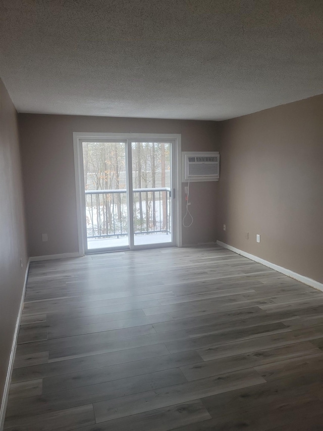 spare room with dark wood-type flooring, a textured ceiling, and an AC wall unit