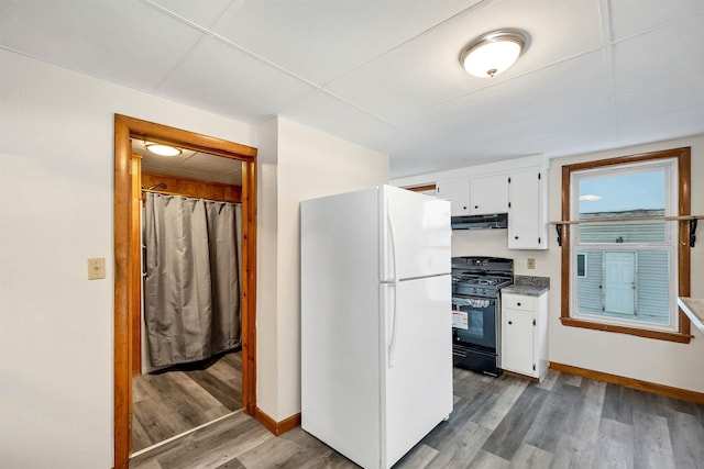 kitchen with white refrigerator, hardwood / wood-style floors, white cabinets, and black range with gas stovetop